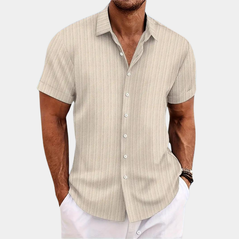 Man wearing a beige short-sleeve shirt with white pants on a light gray background
