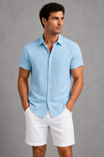 Man wearing a light blue short-sleeve shirt and white shorts against a gray background