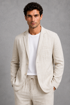 Man wearing a beige linen suit with a white t-shirt against a gray background