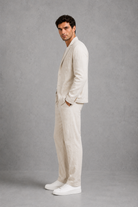 Man wearing a beige suit and white sneakers against a gray background