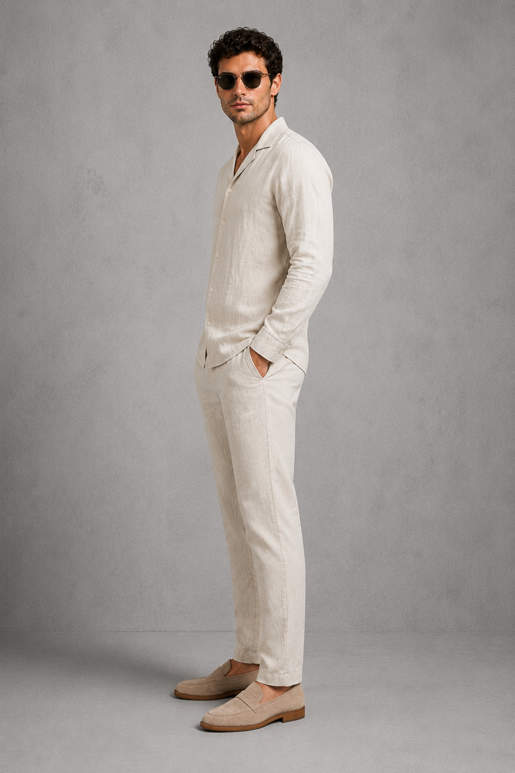 Man wearing a beige linen suit with sunglasses against a gray background