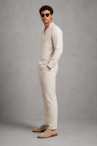 Man wearing a beige linen suit with sunglasses against a gray background