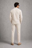 Man wearing a beige linen suit standing against a gray background