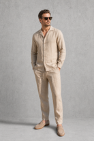 Man wearing a beige linen suit with sunglasses against a gray background