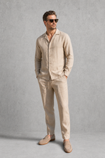 Man wearing a beige linen suit with sunglasses against a gray background