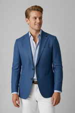 Man wearing a blue blazer over a light blue shirt with white pants on a gray background