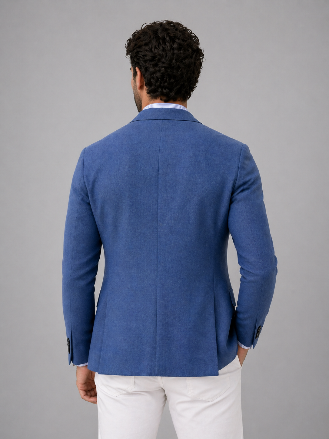 Man wearing a blue blazer and white pants against a gray background