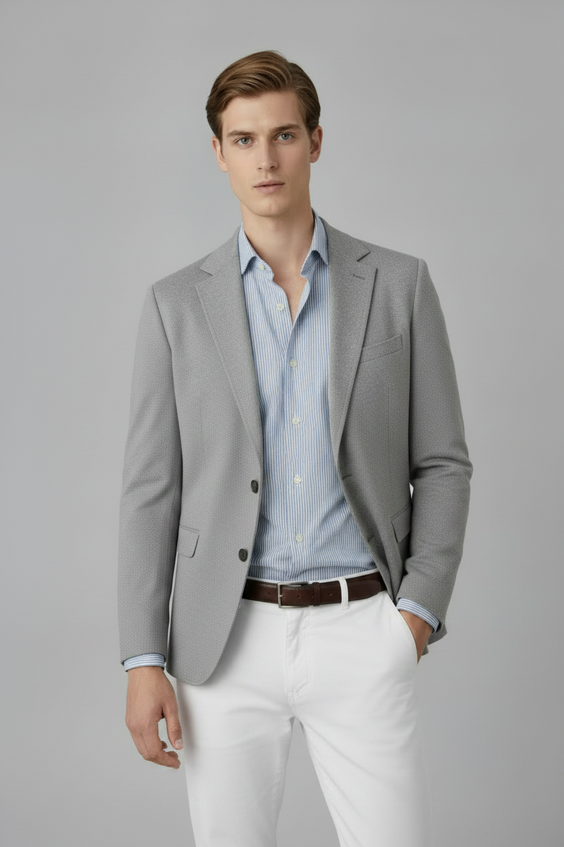 Man wearing a gray blazer over a light blue shirt with white pants on a gray background