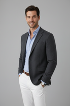 Man wearing a gray blazer over a light blue shirt with white pants on a gray background
