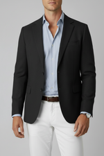 Man wearing a dark blazer, light blue shirt, and white pants against a gray background