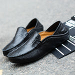 Black leather loafers on a gray surface with a black mat underneath