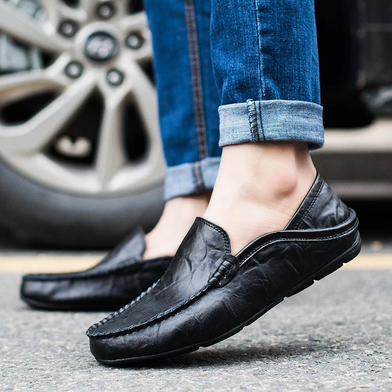 Black leather loafers worn with rolled-up jeans on a street.