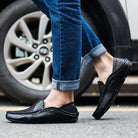 Person wearing black loafers and blue jeans stepping onto a car tire.