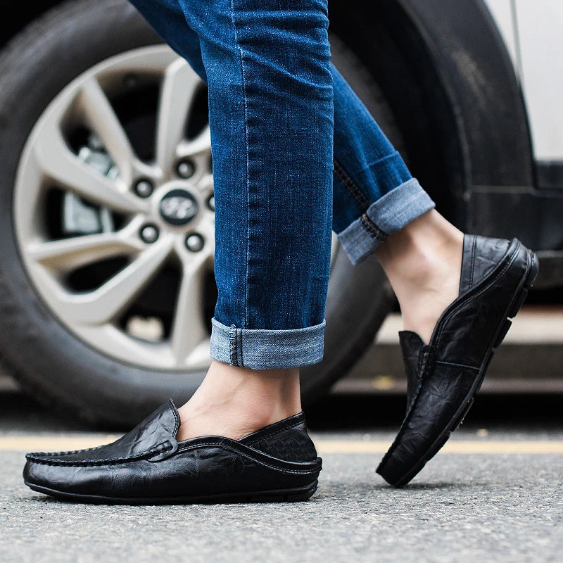 Person wearing black loafers and blue jeans stepping onto a car tire.