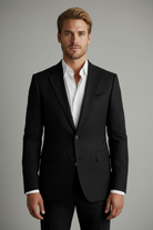 Man wearing a black suit jacket over a white shirt on a gray background