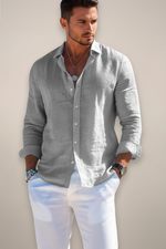 Man wearing a light gray button-up shirt with rolled-up sleeves against a plain background