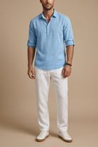 Man wearing a blue linen shirt and white pants against a beige background