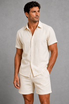 Man wearing a beige linen shirt and shorts against a gray background