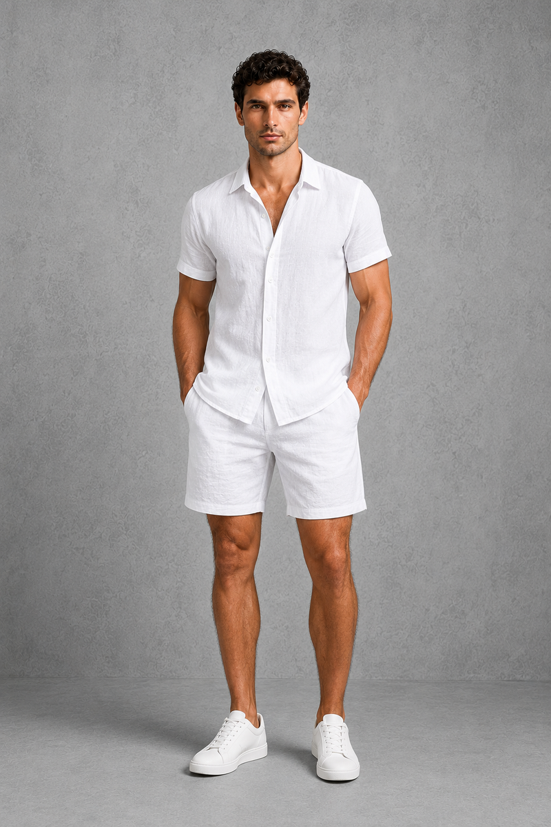 Man wearing a white linen shirt and shorts with white sneakers against a gray background