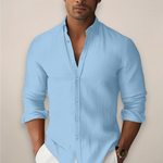 Man wearing a light blue button-up shirt with rolled-up sleeves against a beige background