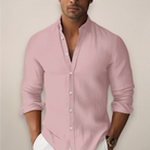 Man wearing a light pink button-up shirt with rolled-up sleeves against a plain background