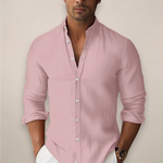 Man wearing a light pink button-up shirt with rolled-up sleeves against a plain background