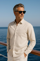 Man in a beige shirt and pants standing on a boat with ocean and clear sky in the background