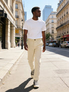 Man walking on a city street wearing a white t-shirt and beige pants.