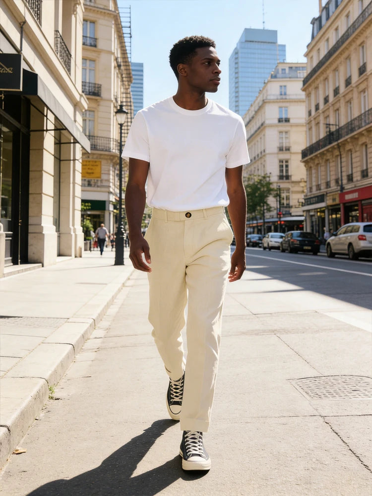 Man walking on a city street wearing a white t-shirt and beige pants.