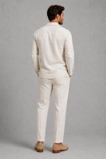Man wearing a beige linen suit standing against a gray background