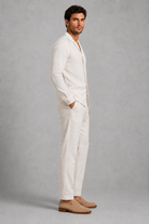 Man wearing a white linen suit with beige shoes on a gray background