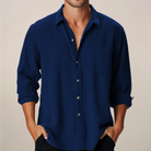 Man wearing a blue button-up shirt with rolled-up sleeves against a beige background
