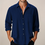 Man wearing a blue button-up shirt with rolled-up sleeves against a beige background