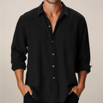 Man wearing a black button-up shirt with rolled-up sleeves against a beige background