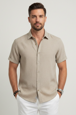 Man wearing a beige short-sleeve shirt with white pants on a light gray background