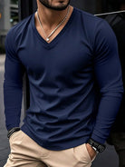 Man wearing a blue long-sleeve shirt and beige pants with a blurred background