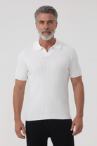 Man wearing a white ribbed polo shirt and black pants on a light gray background