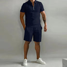 Person wearing a black polo shirt and shorts with white sneakers on a gray background