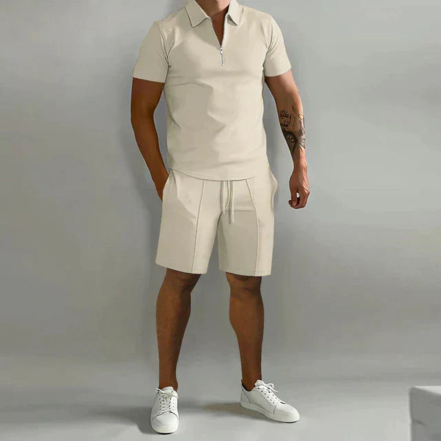 Man wearing a beige polo shirt and shorts with white sneakers on a gray background