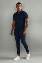 Person wearing a navy blue polo shirt and pants with white sneakers on a plain background