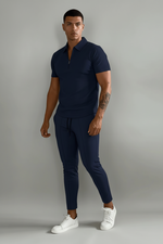 Person wearing a navy blue polo shirt and pants with white sneakers on a plain background