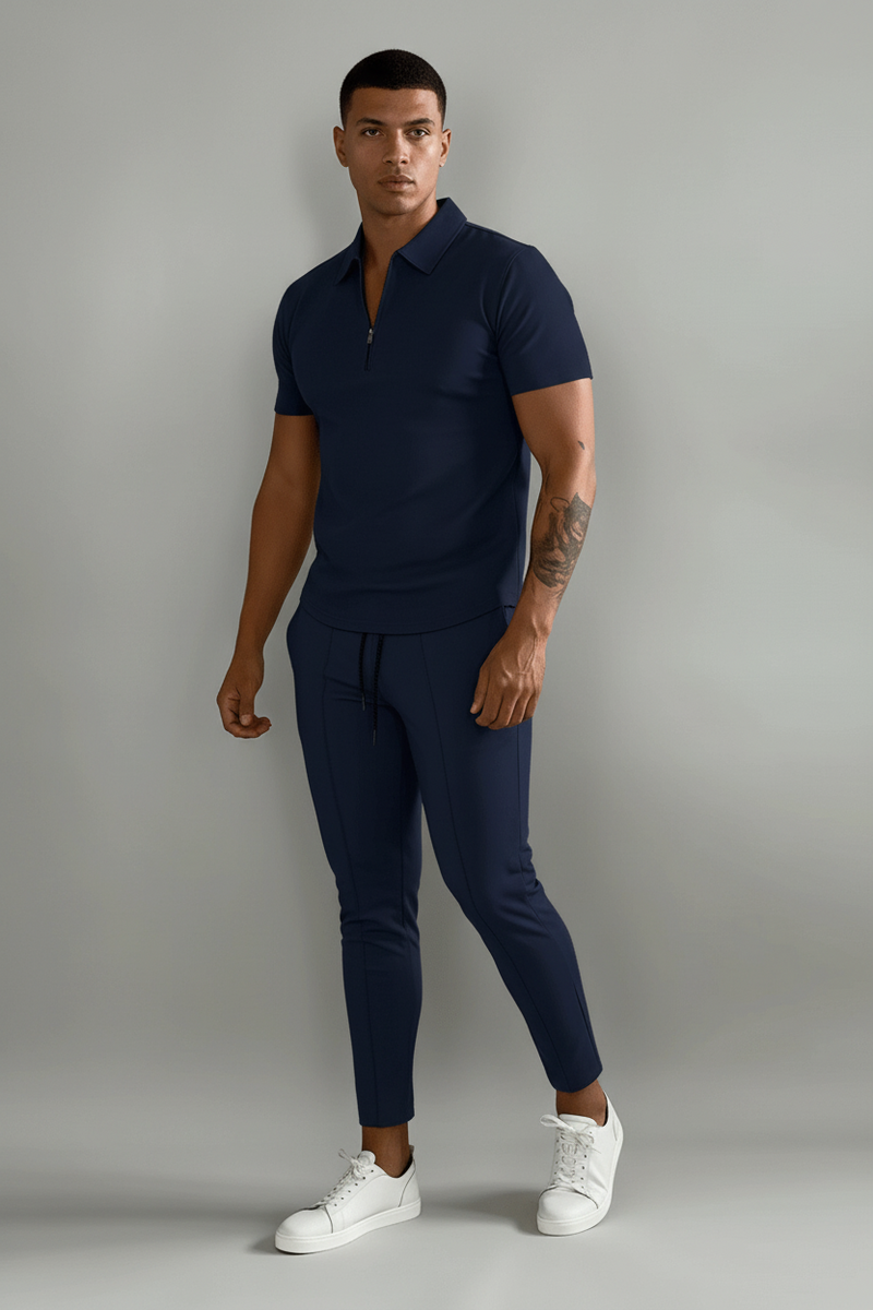 Person wearing a navy blue polo shirt and pants with white sneakers on a plain background