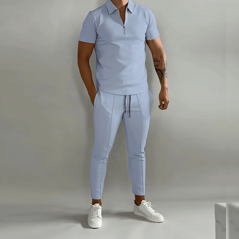 Man wearing a light blue outfit with white sneakers on a plain background