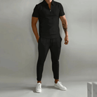 Person wearing a black polo shirt and pants with white sneakers on a plain background