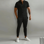 Person wearing a black polo shirt and pants with white sneakers on a plain background