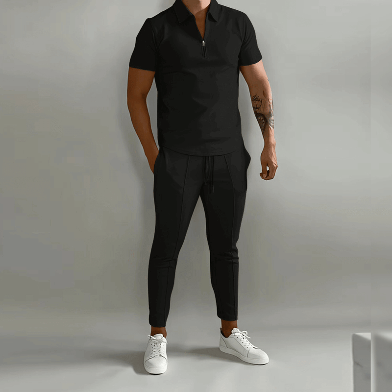 Person wearing a black polo shirt and pants with white sneakers on a plain background
