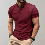 Man wearing a maroon polo shirt and beige pants against a gray background