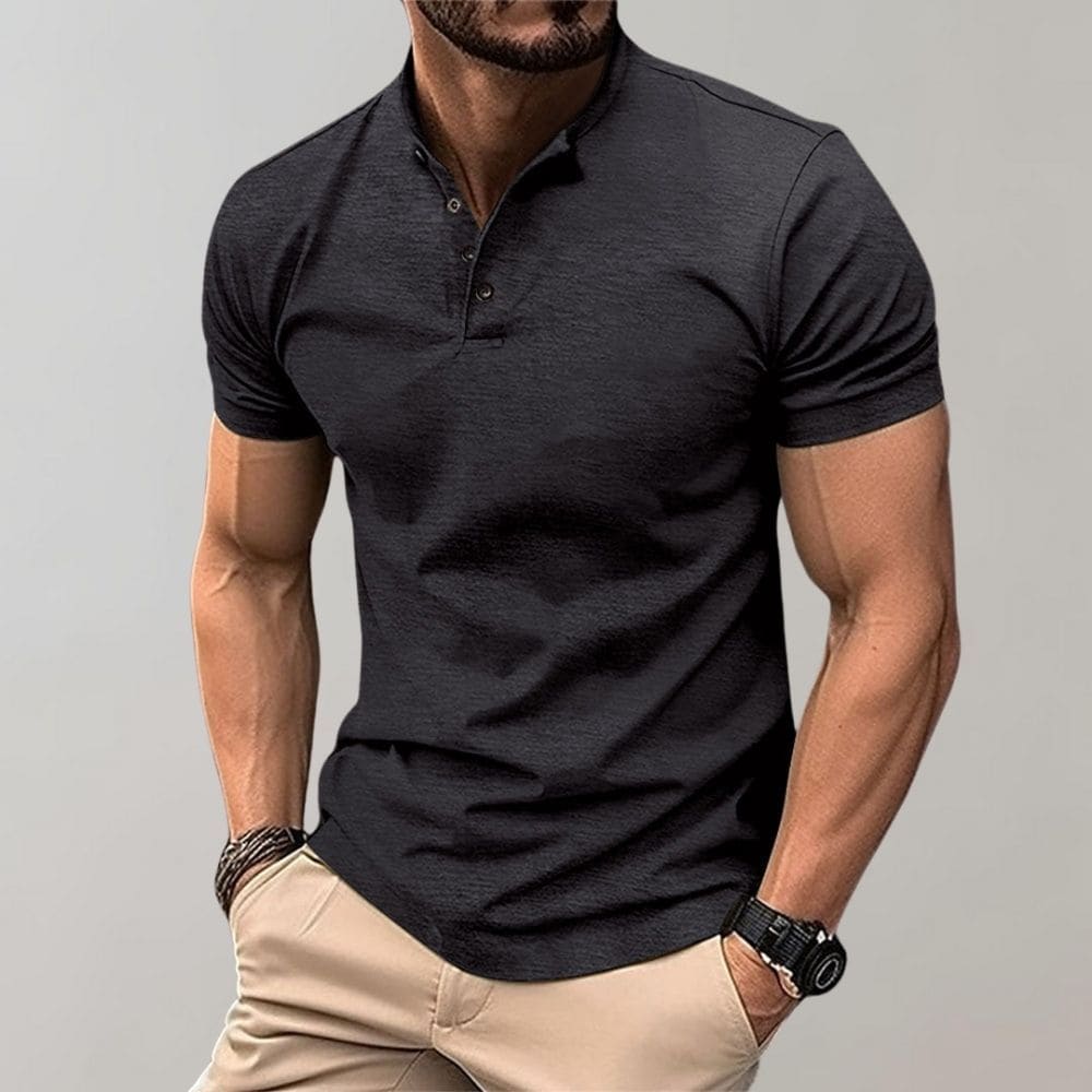 Man wearing a black polo shirt and beige pants against a gray background
