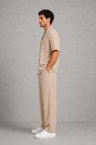 Man wearing a beige outfit with a shirt and pants, standing against a gray background