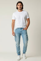 Man wearing a white t-shirt and light blue cargo pants on a plain background